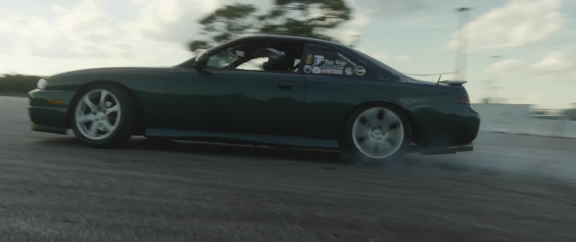 Dark green race car doing doughnuts in an open lot at daytime