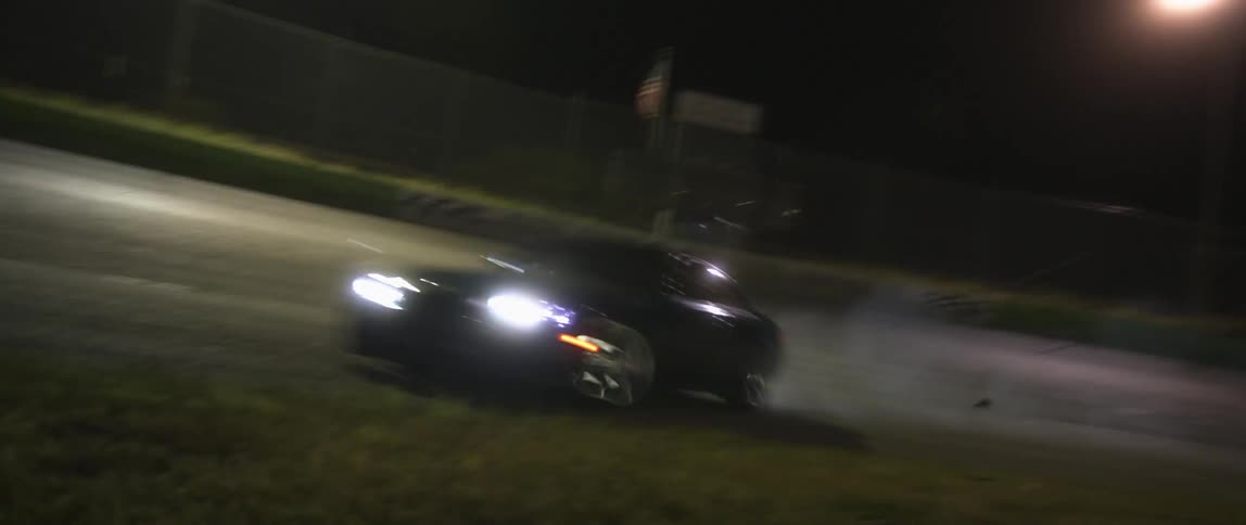 A black sports car races down a race track at night and starts to brake at a turn in the track