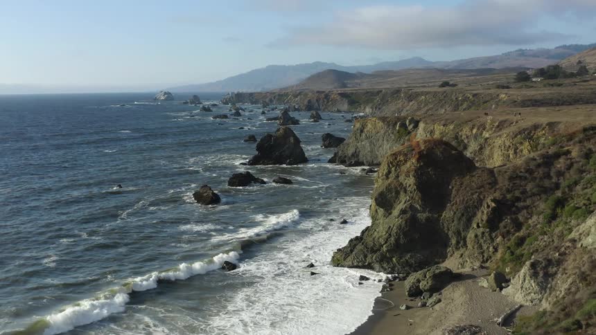 A rocky coast with waves with a mountain range the sky and clouds in the background