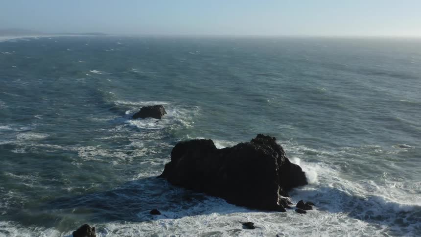 A rocky shore with waves and water with the ocean sky and clouds in the background