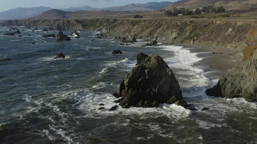 Waves roll in on rocky coast beach and bank with mountains in the distance
