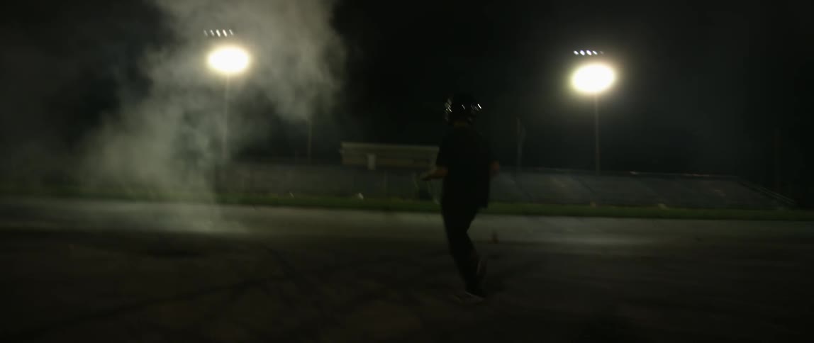 A man with a helmet on runs towards smoke at a race track at night