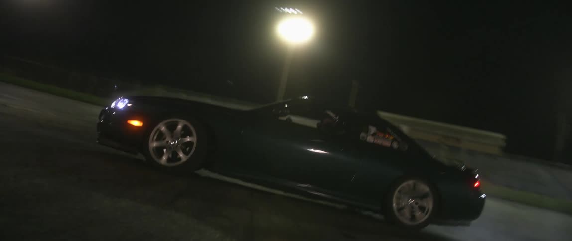 Car drives at night making a sharp turn on road with lights in the background