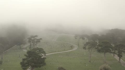 Aerial view of rows of white tombstones on a graveyard under the low clouds