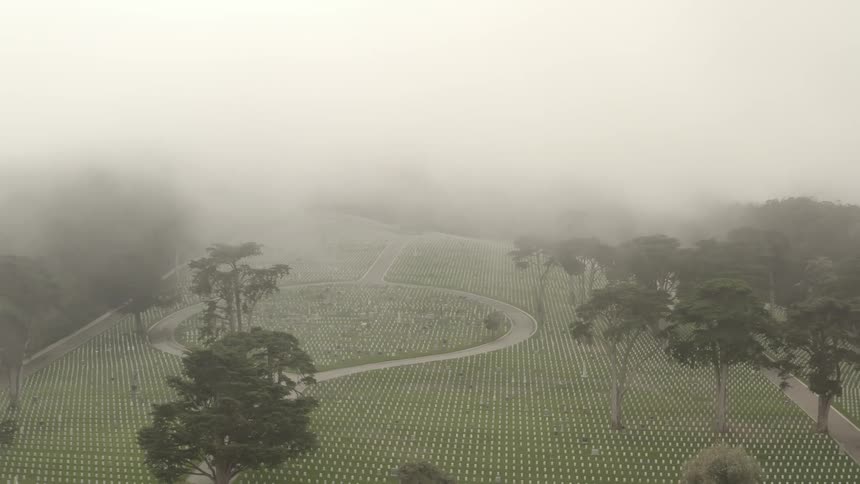 Aerial view of rows of white tombstones on a graveyard under the low clouds
