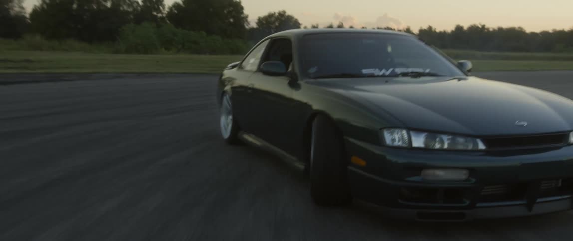 An olive green car drifting on a racing course at sunset