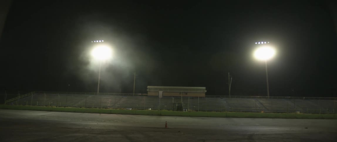 A black sports car drives on a track in front of bleachers at night