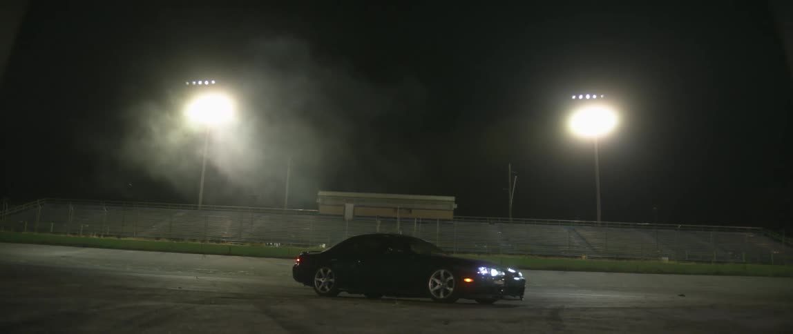 Black sports car parked on a race track at night turns on the headlights