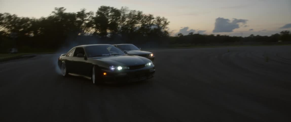Two cars are driving around a curve on a track outdoors at night