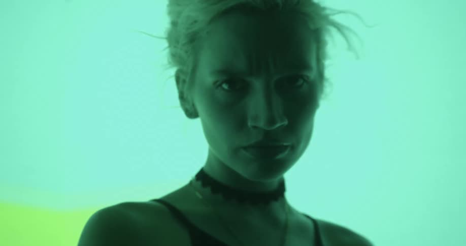 A model walks forward and backward in front of a digital screen flashing different colors and shapes