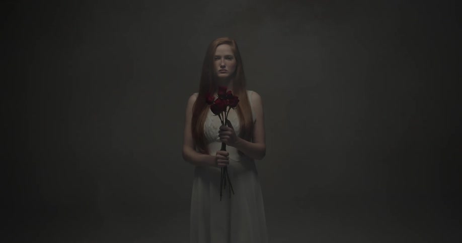 Woman holding red roses with both of her hands while fog comes up from the left