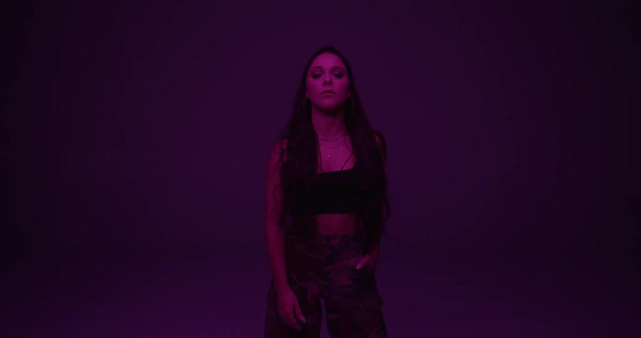 Woman with long wavy hair stands and faces the camera with eye contact on the purple background in studio