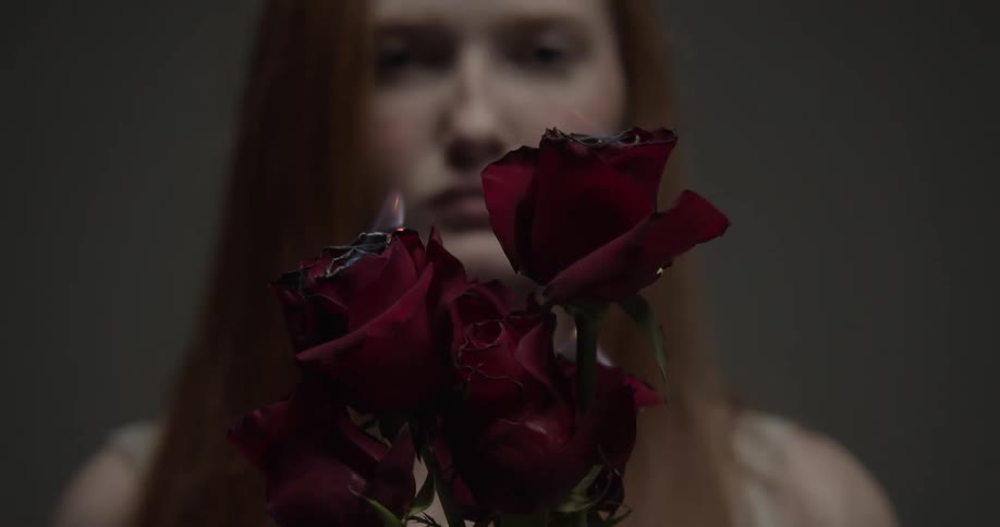A young woman stares into the camera while holding a bouquet of burning burgundy roses