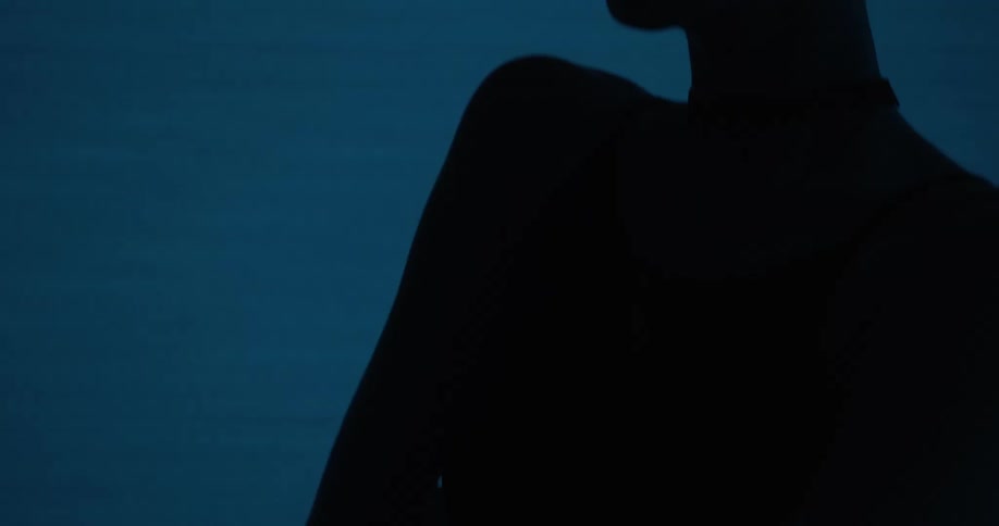 A blonde woman stands with her arms crossed in front of her in front of lights that change colors with shadows