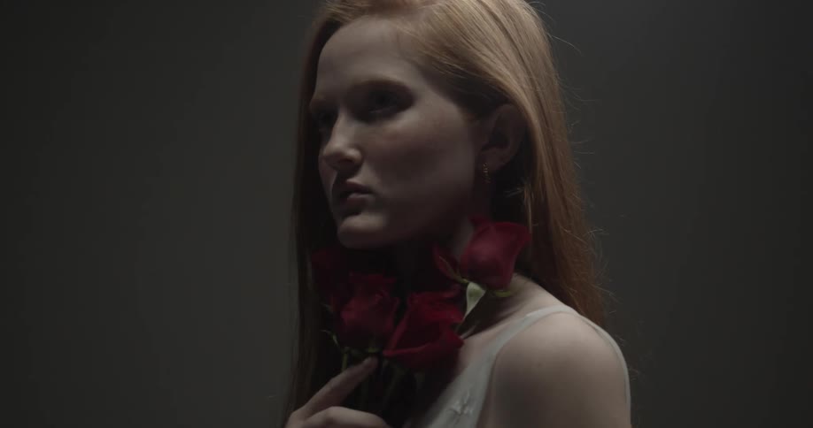 Red haired woman strokes roses along neck then turns her head