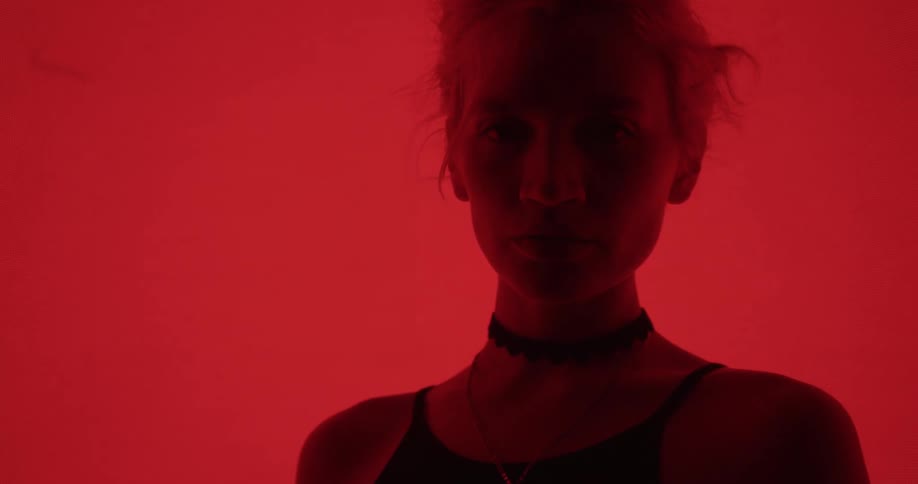 Young blonde woman standing in front of a colorful digital display turns around and looks at the camera