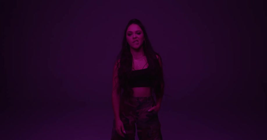 Young woman standing in a room under purple light gestures at the camera