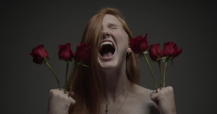 A woman holds roses between her fingers and yells