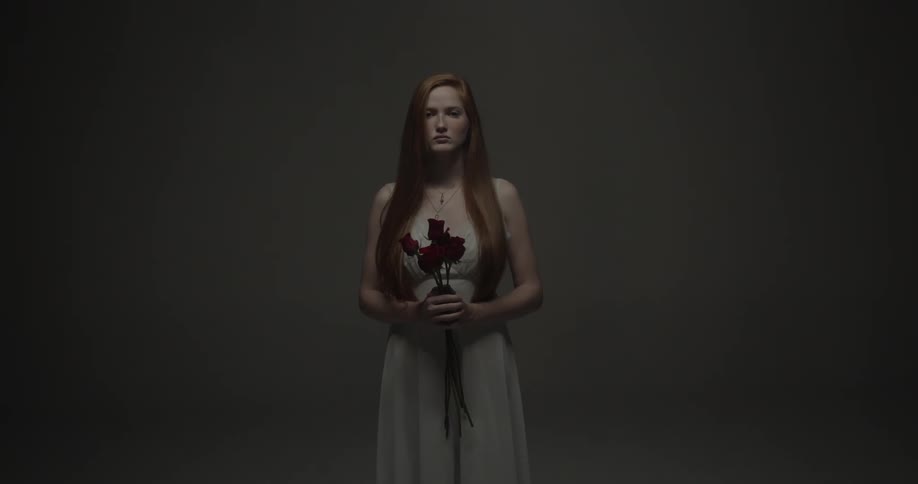 Woman holding a small bouquet of red roses standing in a dark grey room