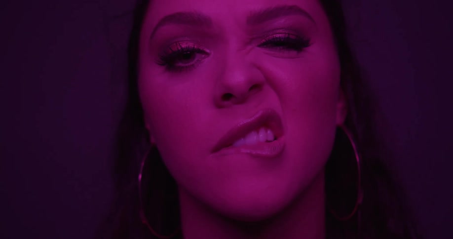 A woman looking at the camera bites her lips and makes faces under a purple light