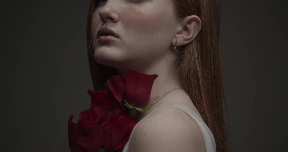 A young woman holds roses and runs them slowly down her face and body
