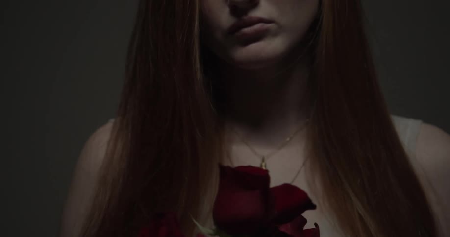 A young woman with red hair poses with a half dozen red roses