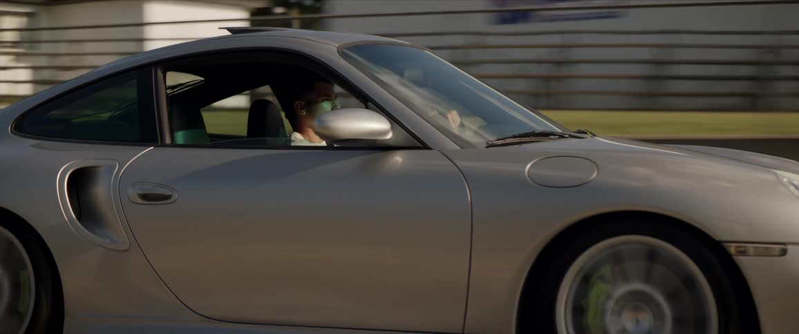 A man drives a silver sports car on a road during the day