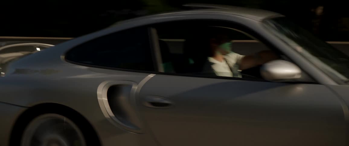 A man drives a luxury sports car along a road at a high speed