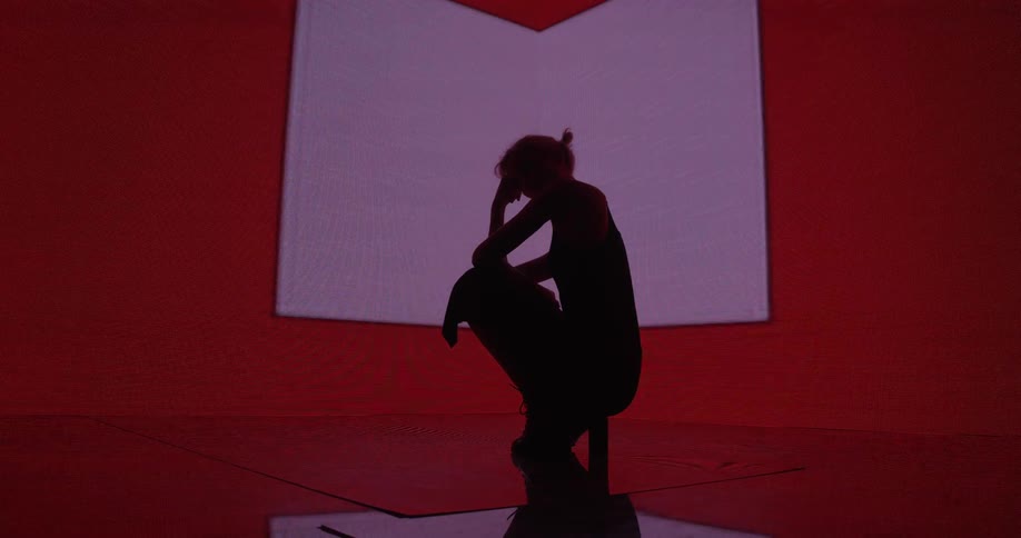 A model poses while crouched in front of a large projector screen as various shapes flash behind her