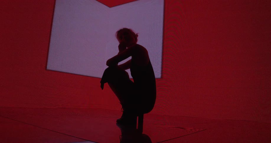 A model crouches down while posing in front of a digital screen with flashing colorful shapes