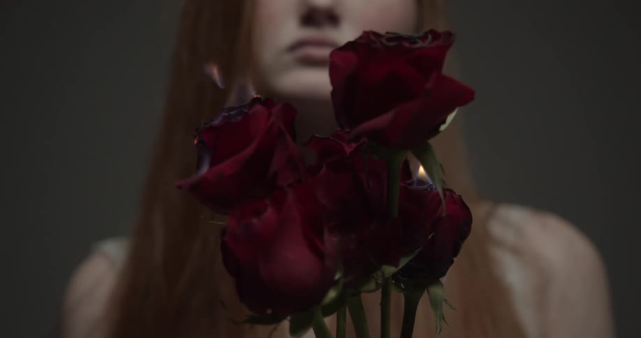 A woman poses holding a bunch of red roses that are on fire and burning
