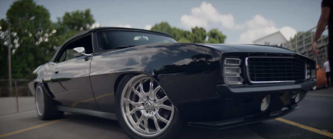 Man closes the hood of a sports coupe car parked next to a stadium