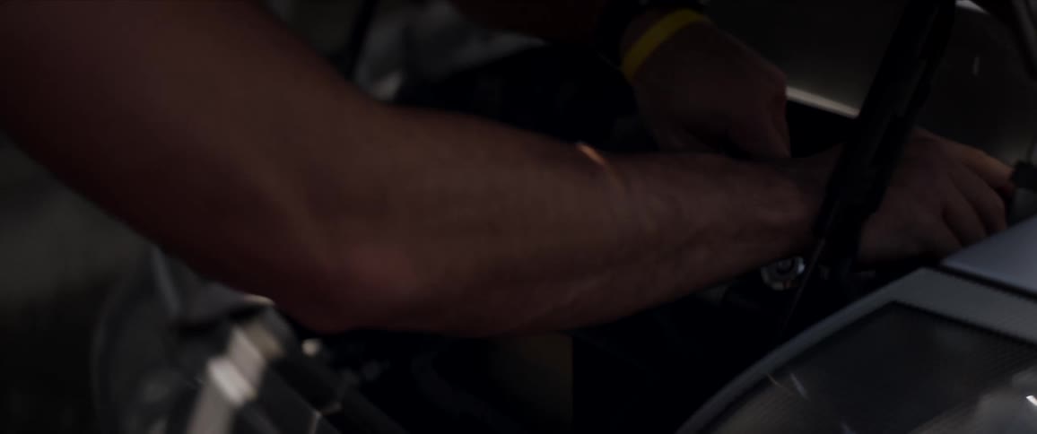 A man with a tool working on a vehicle with trees in the background