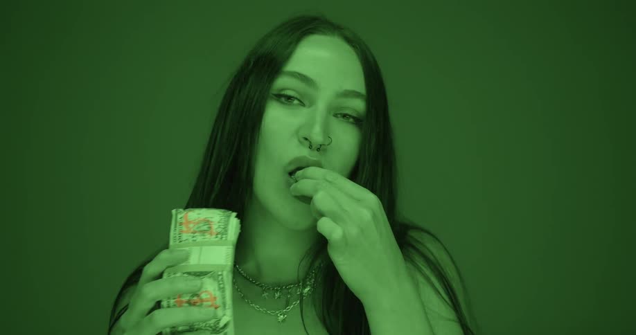 A woman holds up paper currency in her hands and places a bill in her mouth and chews it