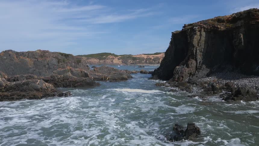 Water with waves against a shoreline with rocks and a blue sky