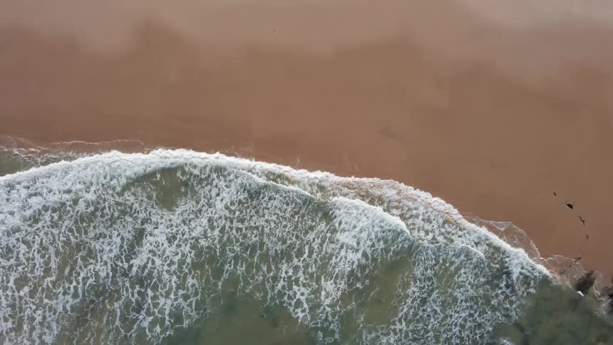 Aerial of waves crashing into the shoreline on a sandy beach