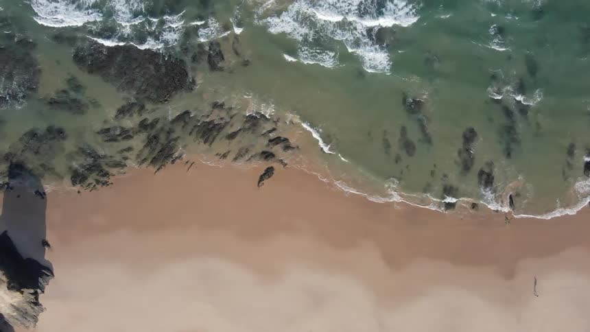 Top down aerial view of the black rocks in the coastline of a beach