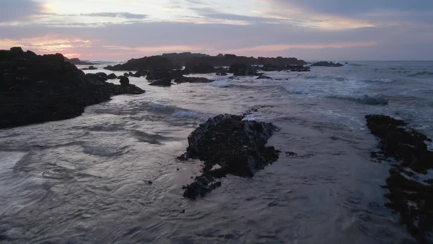 An aerial view of ocean waves flowing towards a coastline at sunset