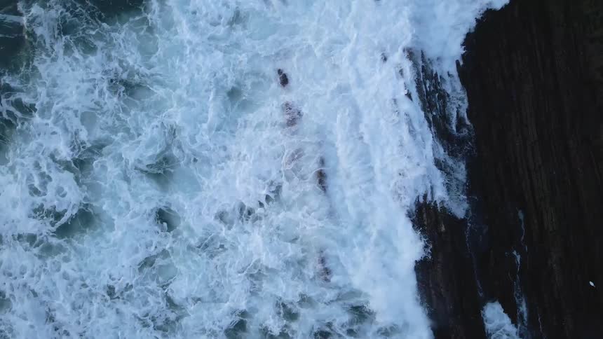 Aerial view of sea waves crashing on the jagged rocks on the coast line