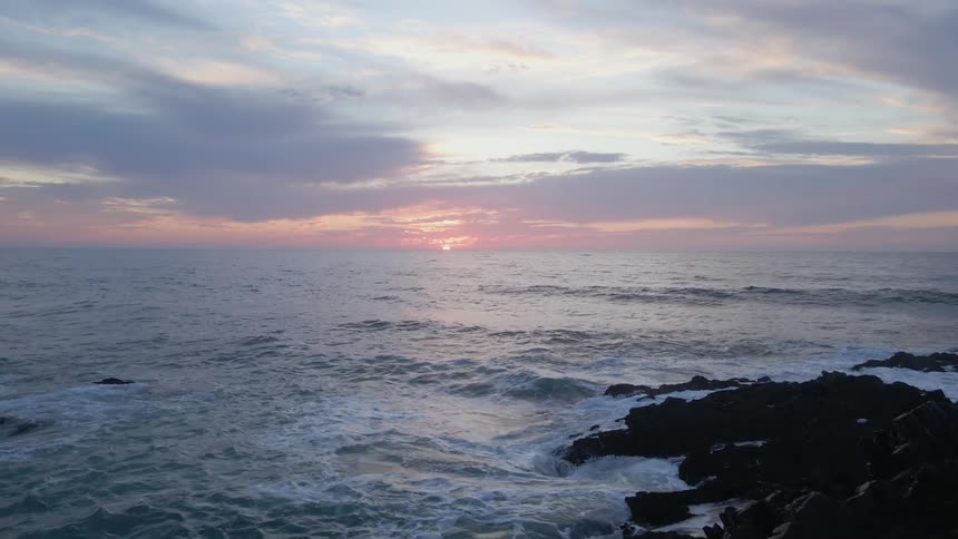 Aerial view of sea waves crashing rocky shore at sunset
