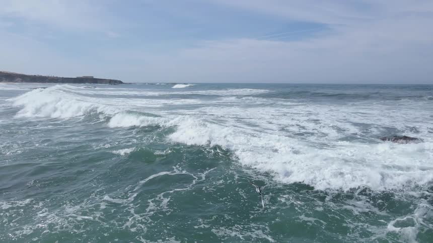 Waves crash steadily onto large rocks in the ocean