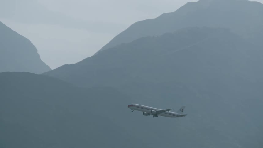 An airplane rises into the clouds between mountains and an airport