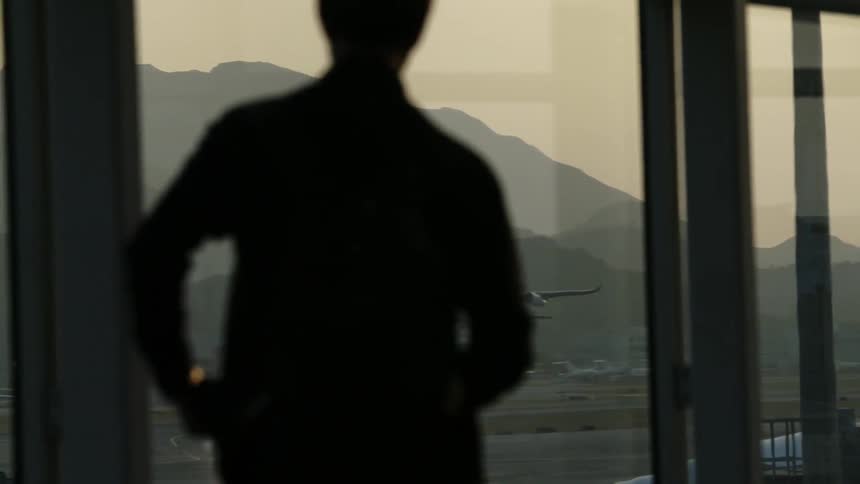 People standing around an airport window as a plane takes off