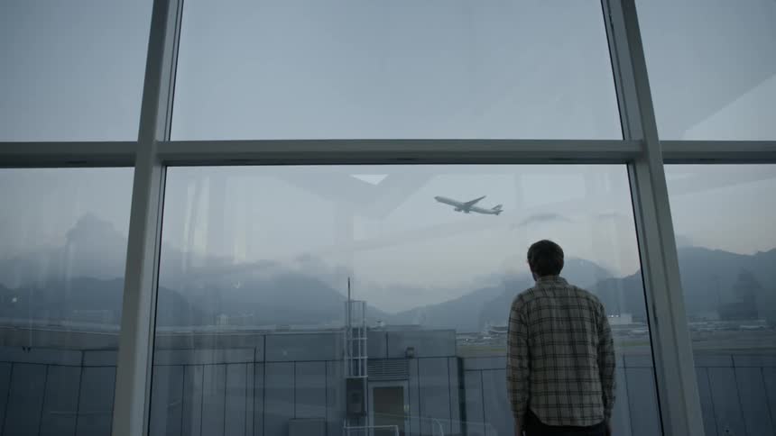 Man standing in airport watching a plane fly off