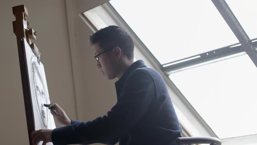 A man is drawing with charcoal on a canvas