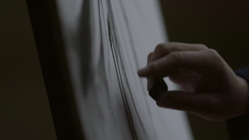 Close up of a hand using charcoal to draw on a canvas