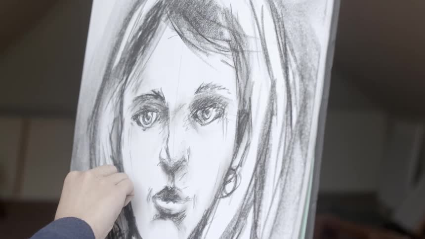 A person is drawing with charcoal on a canvas