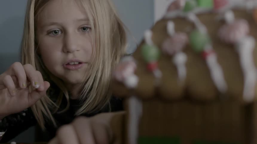 A young girl looks at a gingerbread house on the table