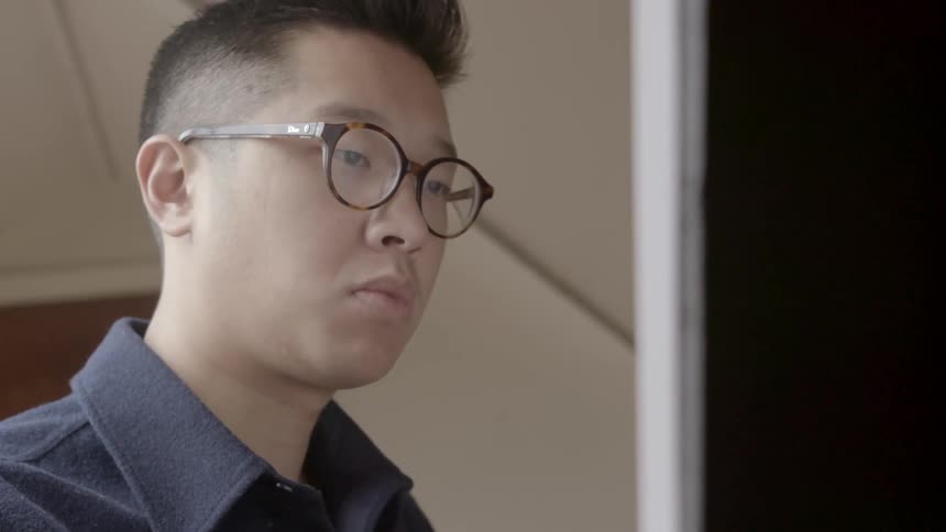 An asian man stands in front of an easel and paints
