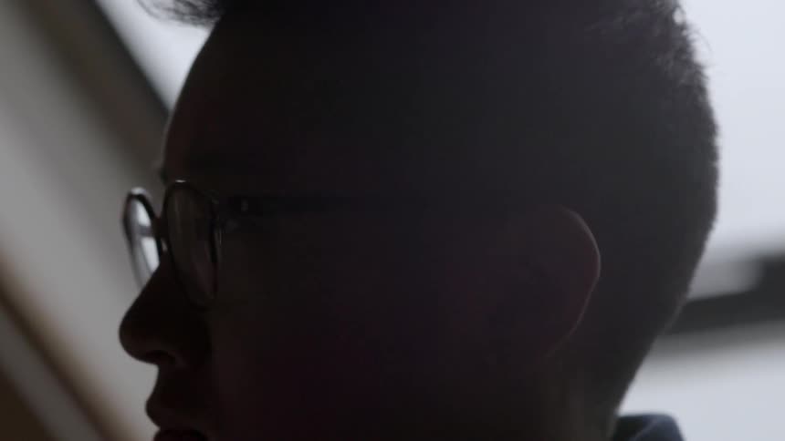 An asian man in profile in a room with a large window